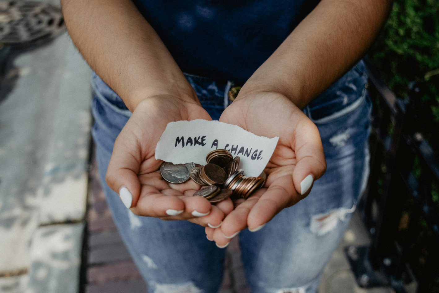 Handen met munten en een briefje met 'make a change' — doneren aan een goed doel begint bij betrokkenheid, niet bij het bedrag.